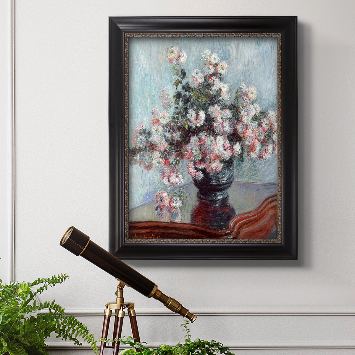 Impressionist chrysanthemum floral painting by Claude Monet in an ornate black frame with gilded inner detail displayed in a light-toned interior setting.