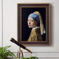 Iconic portrait of a girl wearing a pearl earring by Johannes Vermeer in an ornate bronzed mahogany wood frame displayed in a light-toned interior setting.