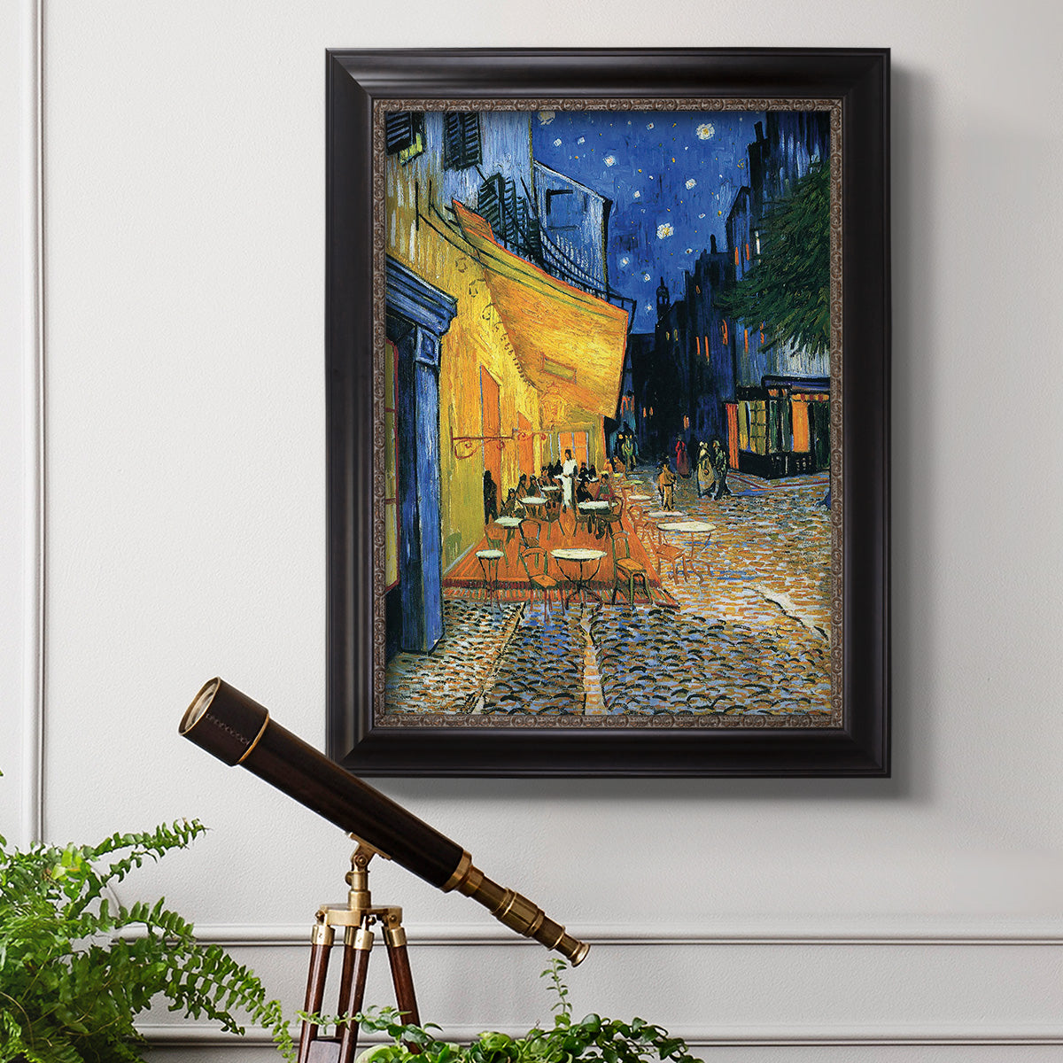 Impressionist night café street scene by Vincent van Gogh in an ornate black frame with gilded inner detail displayed in a light-toned interior setting.