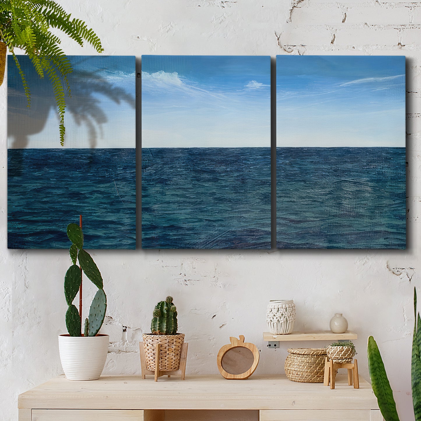 Three-panel canvas wall art featuring open water landscape with wide horizon, displayed in a boho-chic entryway above a console table.