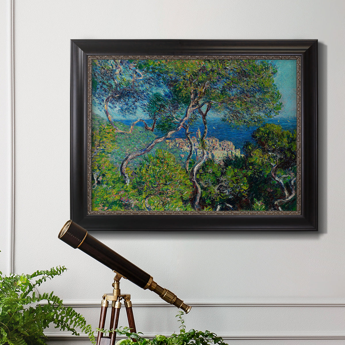 Impressionist Mediterranean coastal landscape by Claude Monet in an ornate black frame with gilded inner detail displayed in a light-toned interior setting.
