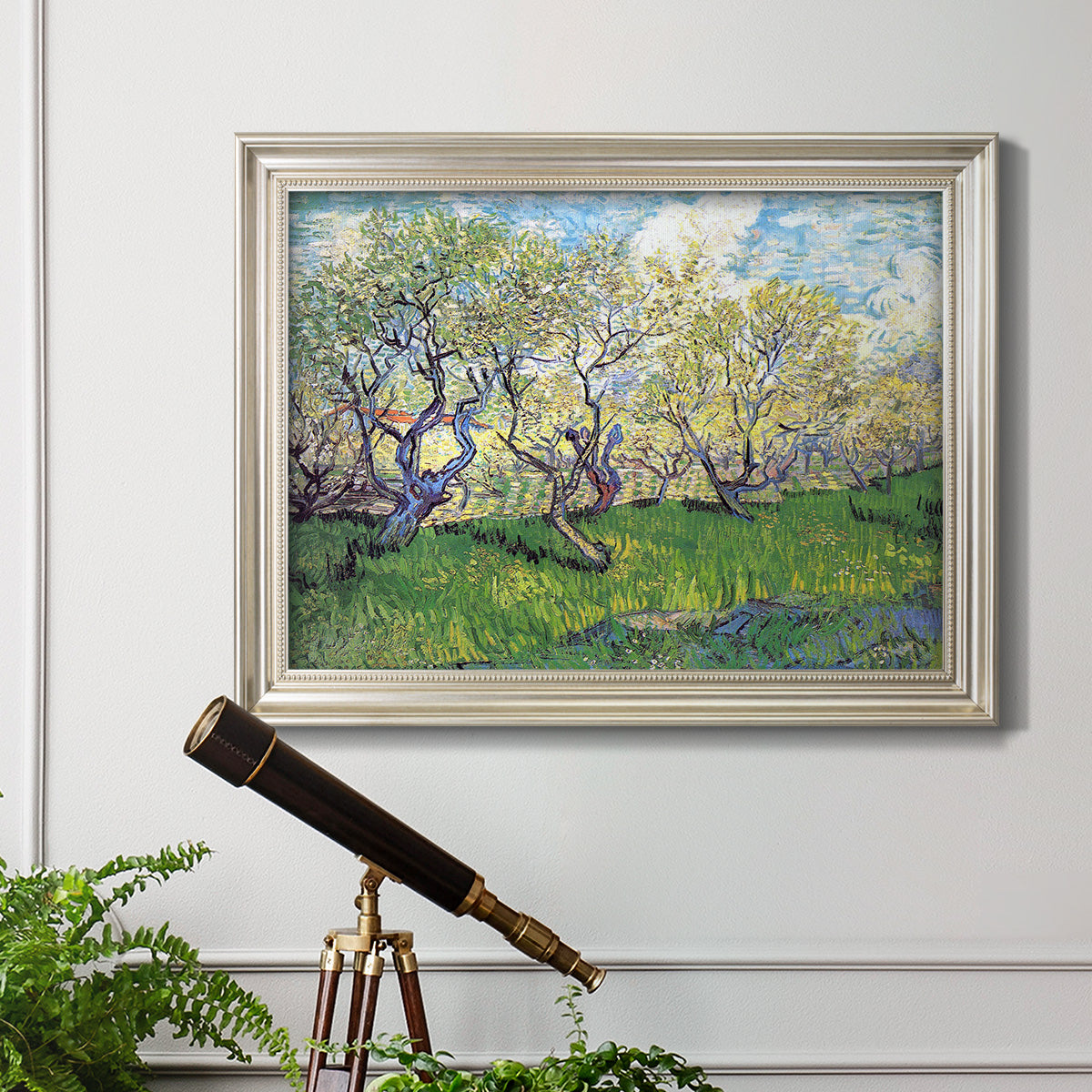 Impressionist spring orchard landscape by Vincent van Gogh in an ornate champagne frame displayed in a light-toned interior setting.