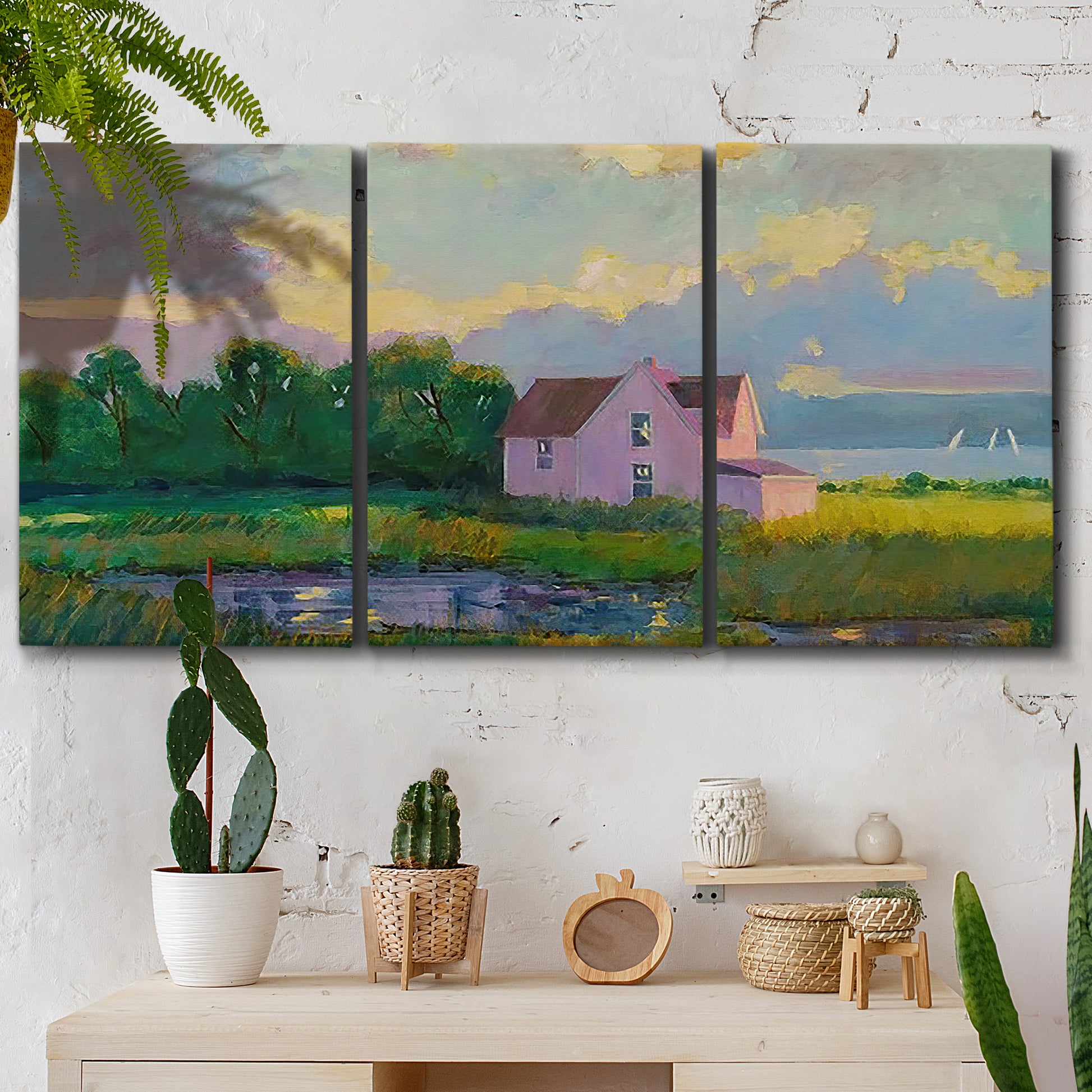Three-panel canvas wall art featuring farmhouse near coastline landscape, displayed in a boho-chic entryway above a console table.