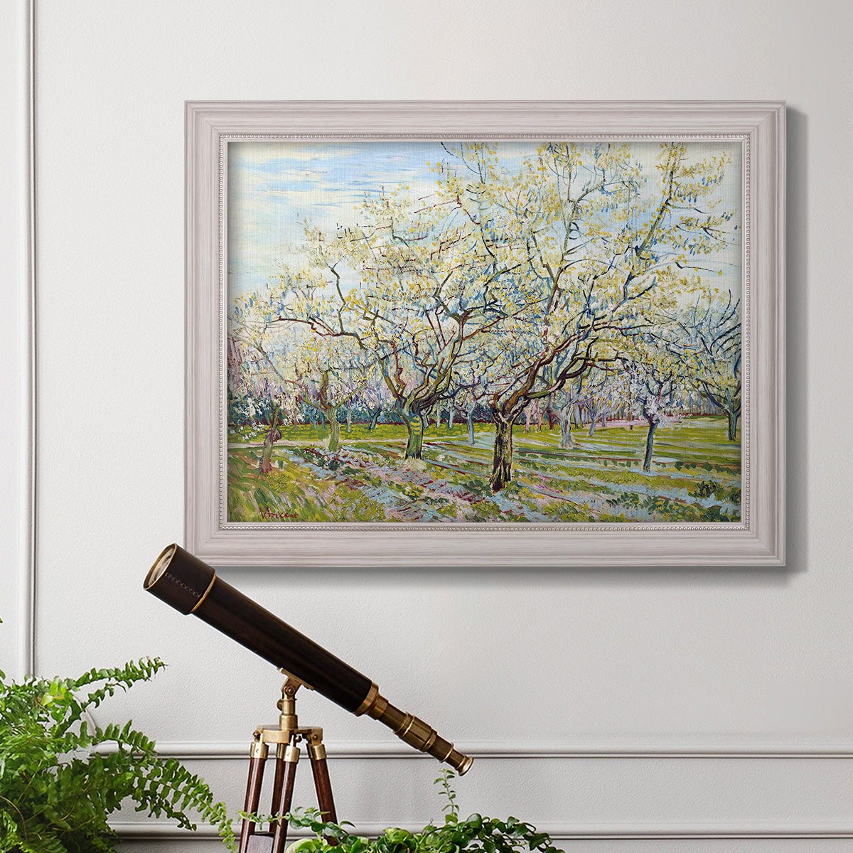 Impressionist white-blossomed orchard landscape by Vincent van Gogh in an ornate weathered white frame displayed in a light-toned interior setting.