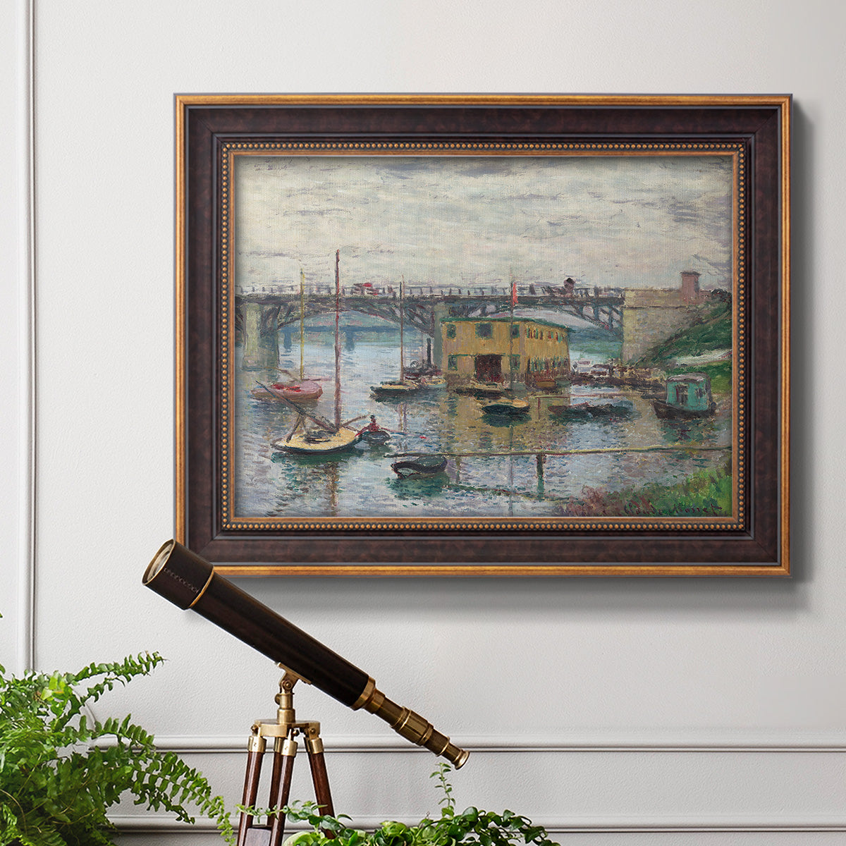 Impressionist river bridge scene on an overcast day by Claude Monet in an ornate bronzed mahogany wood frame displayed in a light-toned interior setting.