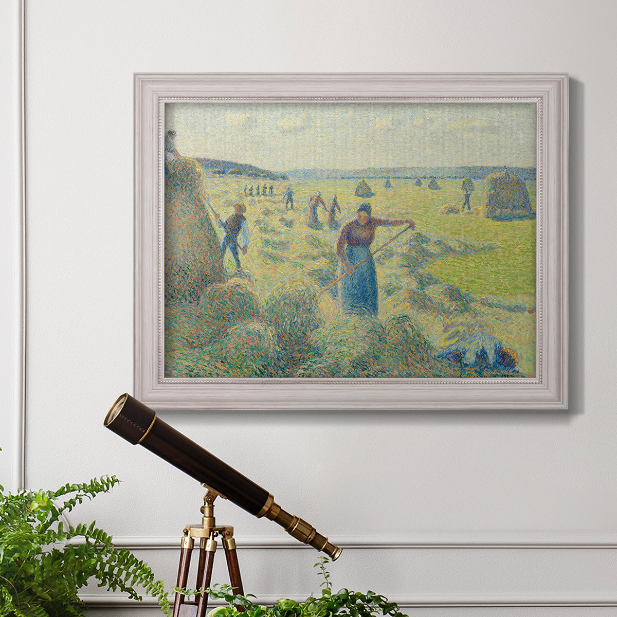 Impressionist rural hay harvest landscape by Camille Pissarro in an ornate weathered white frame displayed in a light-toned interior setting.