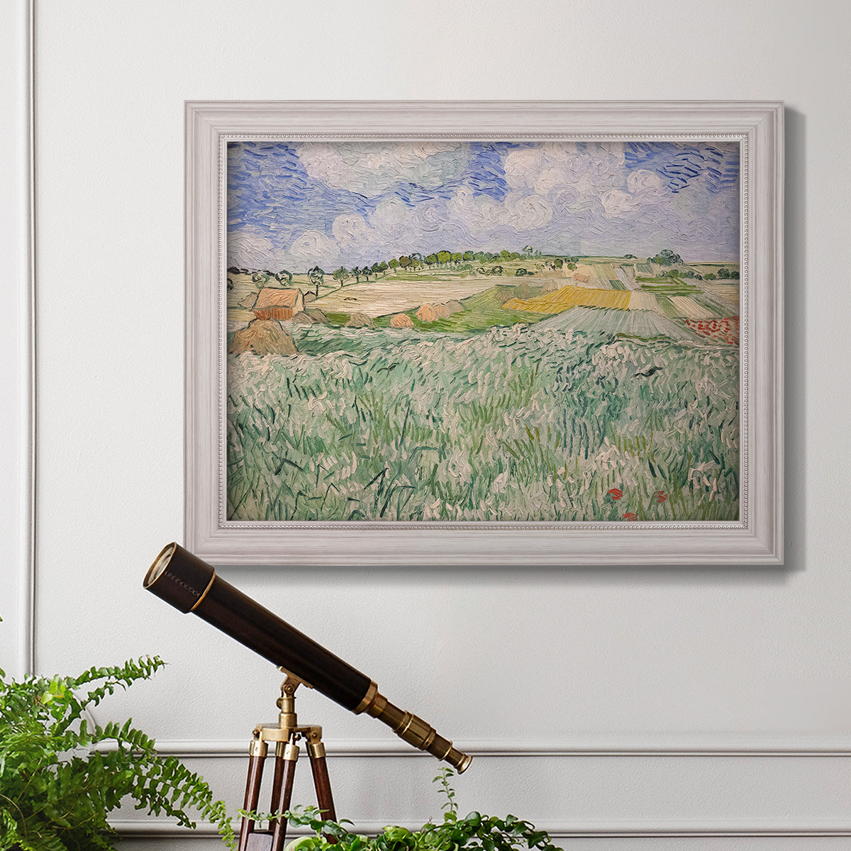 Impressionist countryside landscape near Auvers by Vincent van Gogh in an ornate weathered white frame displayed in a light-toned interior setting.