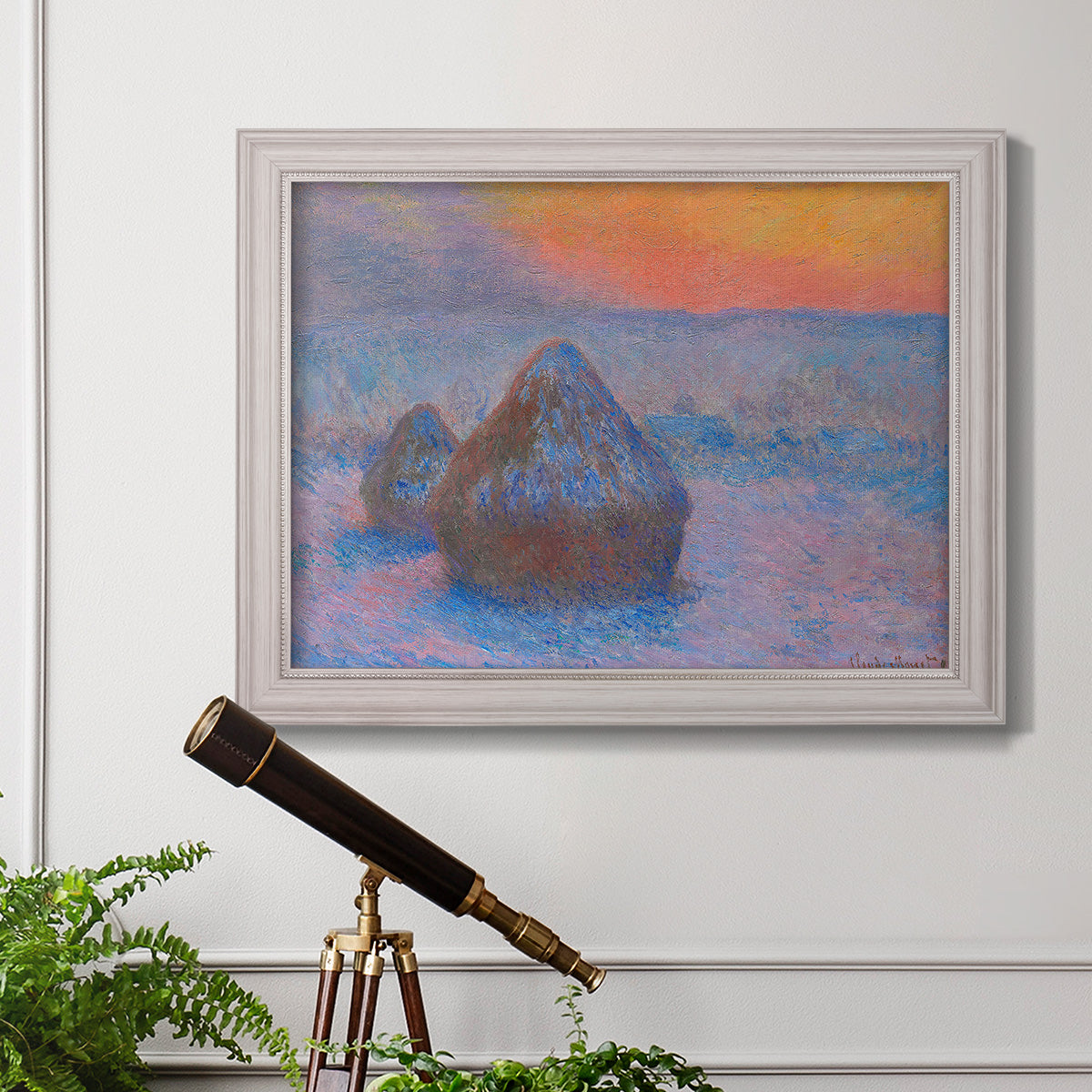 Impressionist haystack scene at sunset by Claude Monet in an ornate weathered white frame displayed in a light-toned interior setting.