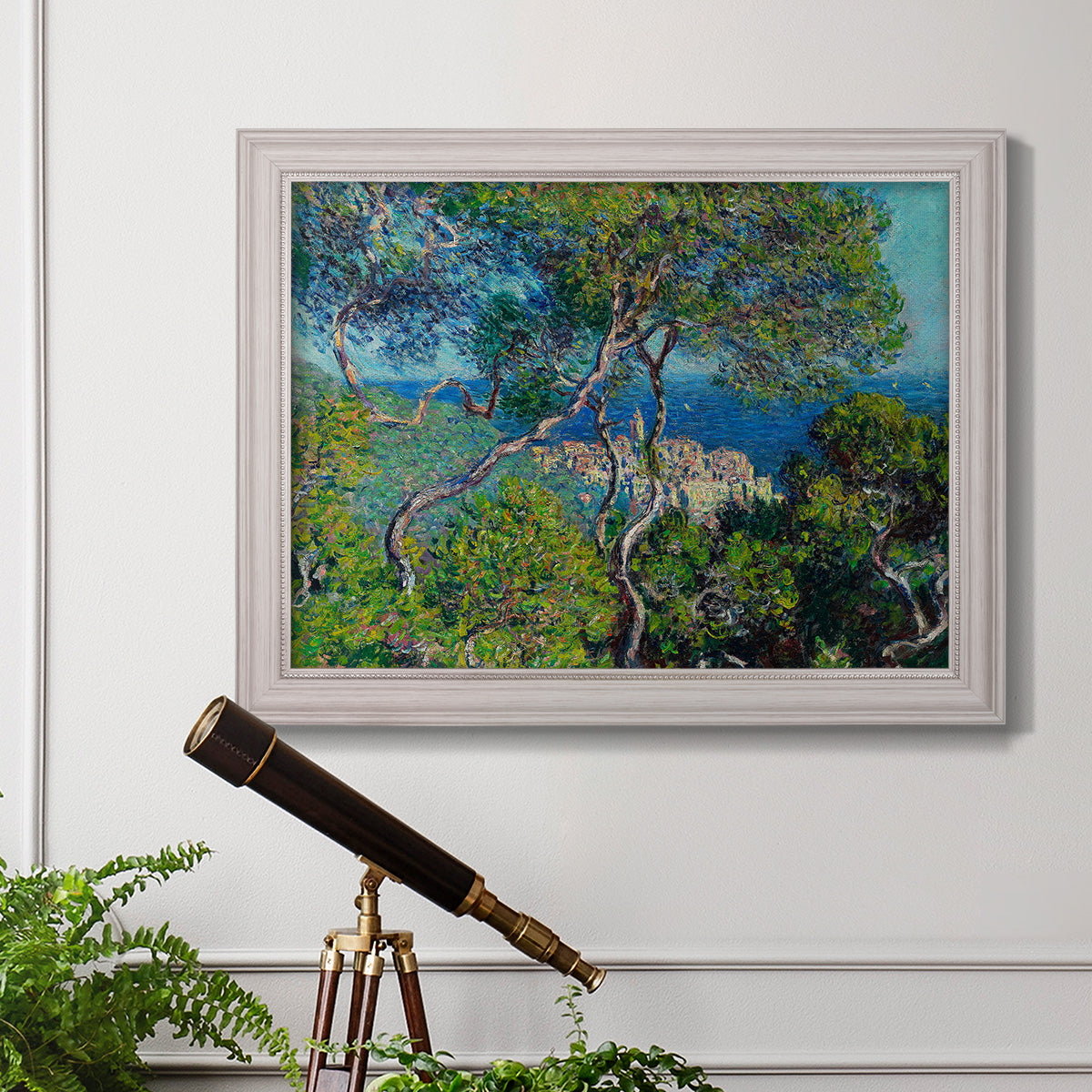 Impressionist Mediterranean coastal landscape by Claude Monet in an ornate weathered white frame displayed in a light-toned interior setting.