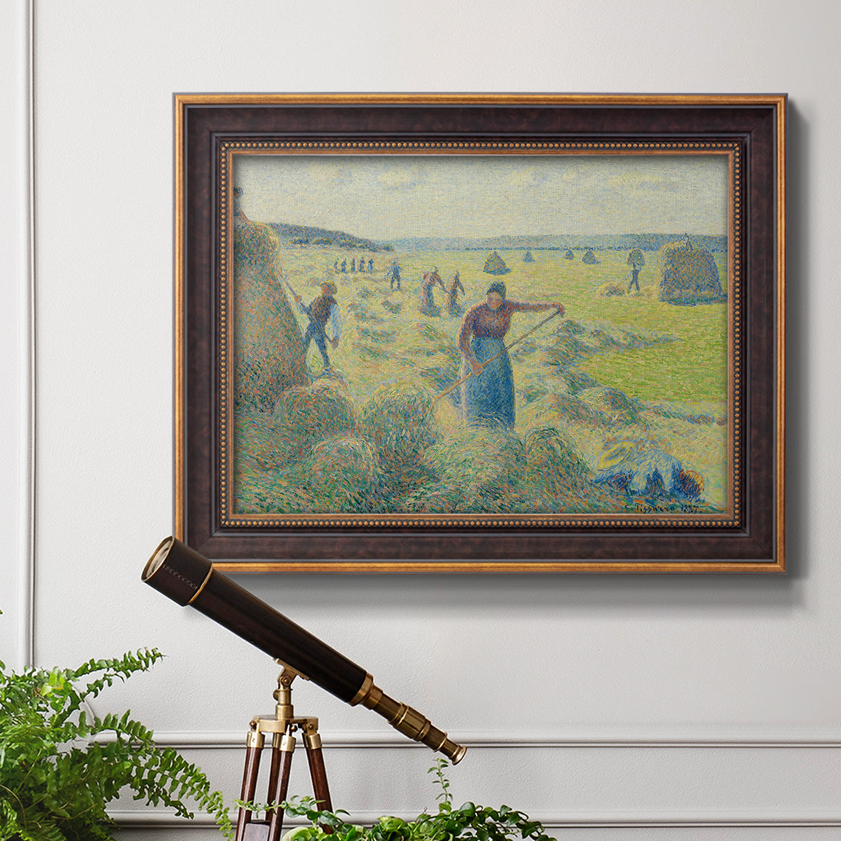 Impressionist rural hay harvest landscape by Camille Pissarro in an ornate bronzed mahogany wood frame displayed in a light-toned interior setting.