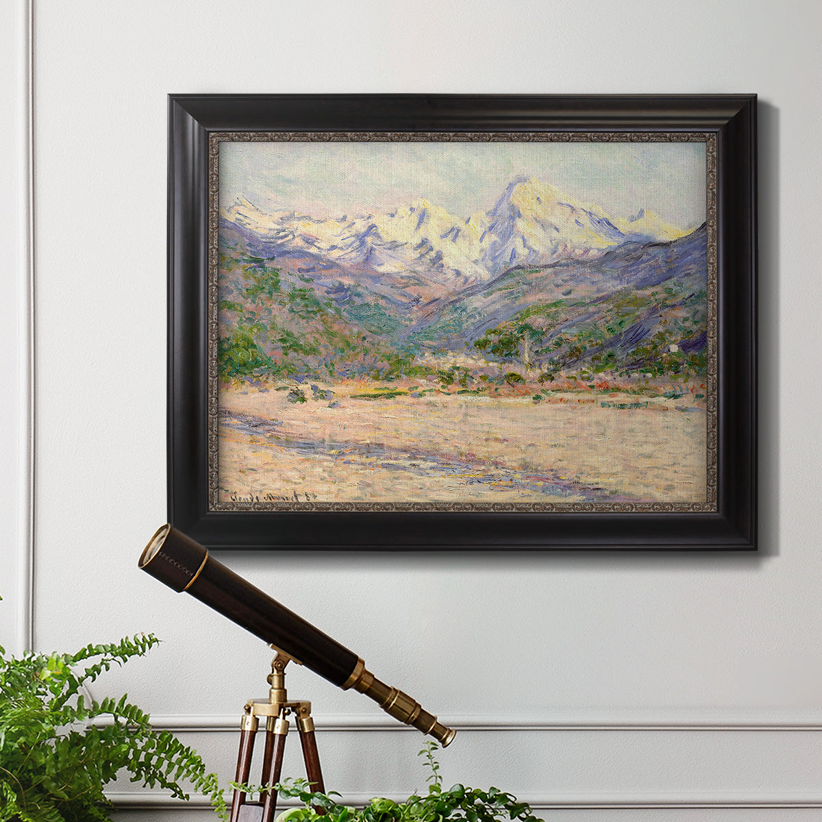 Impressionist valley landscape in southern France by Claude Monet in an ornate black frame with gilded inner detail displayed in a light-toned interior setting.
