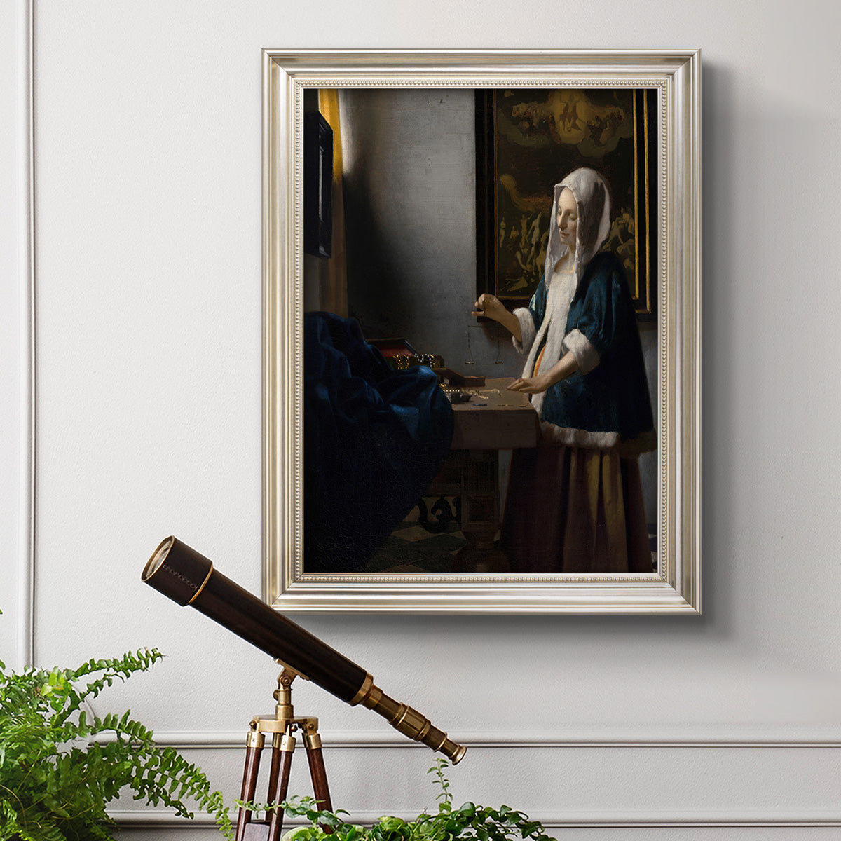 Quiet interior genre scene of a woman with scales by Johannes Vermeer in an ornate champagne frame displayed in a light-toned interior setting.