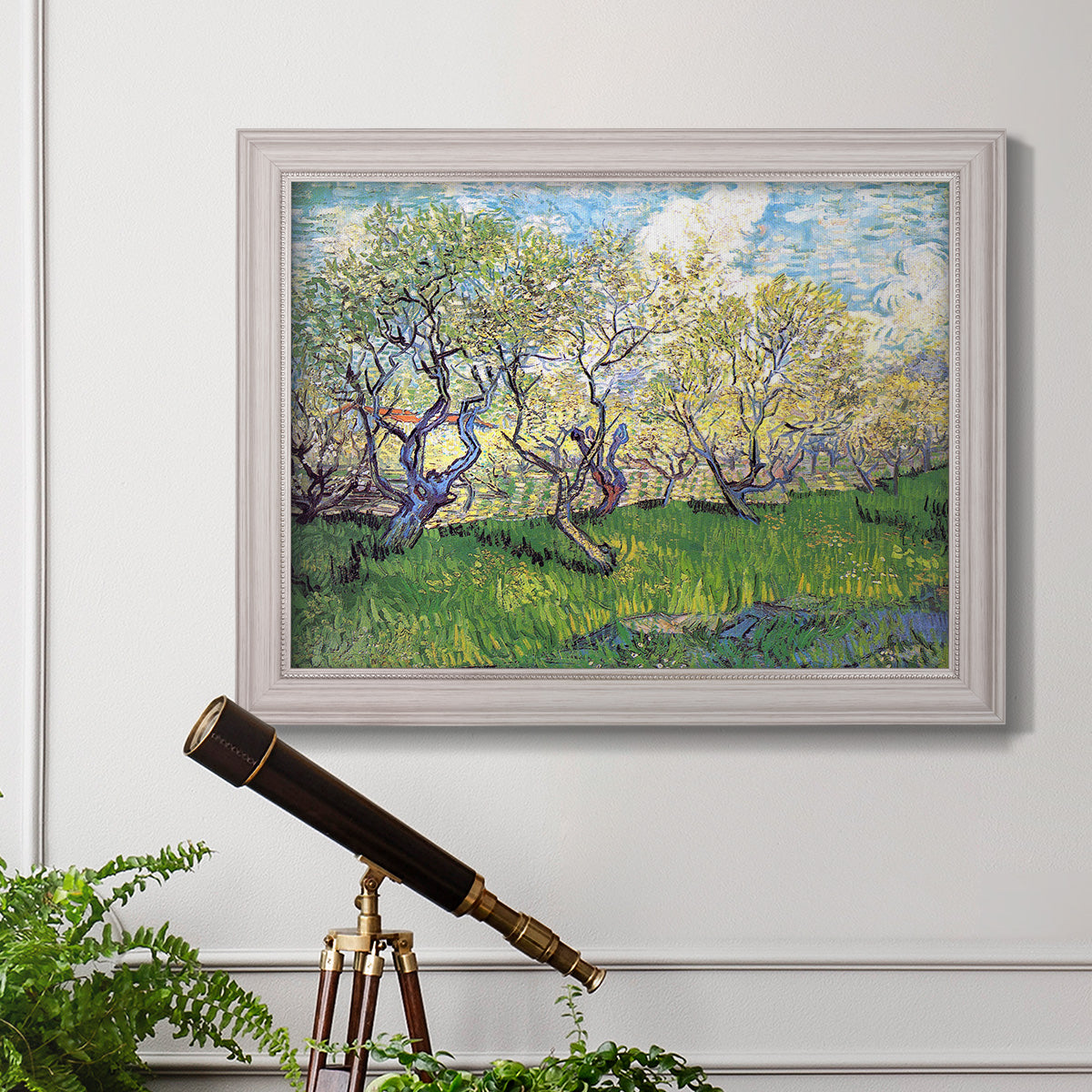 Impressionist spring orchard landscape by Vincent van Gogh in an ornate weathered white frame displayed in a light-toned interior setting.