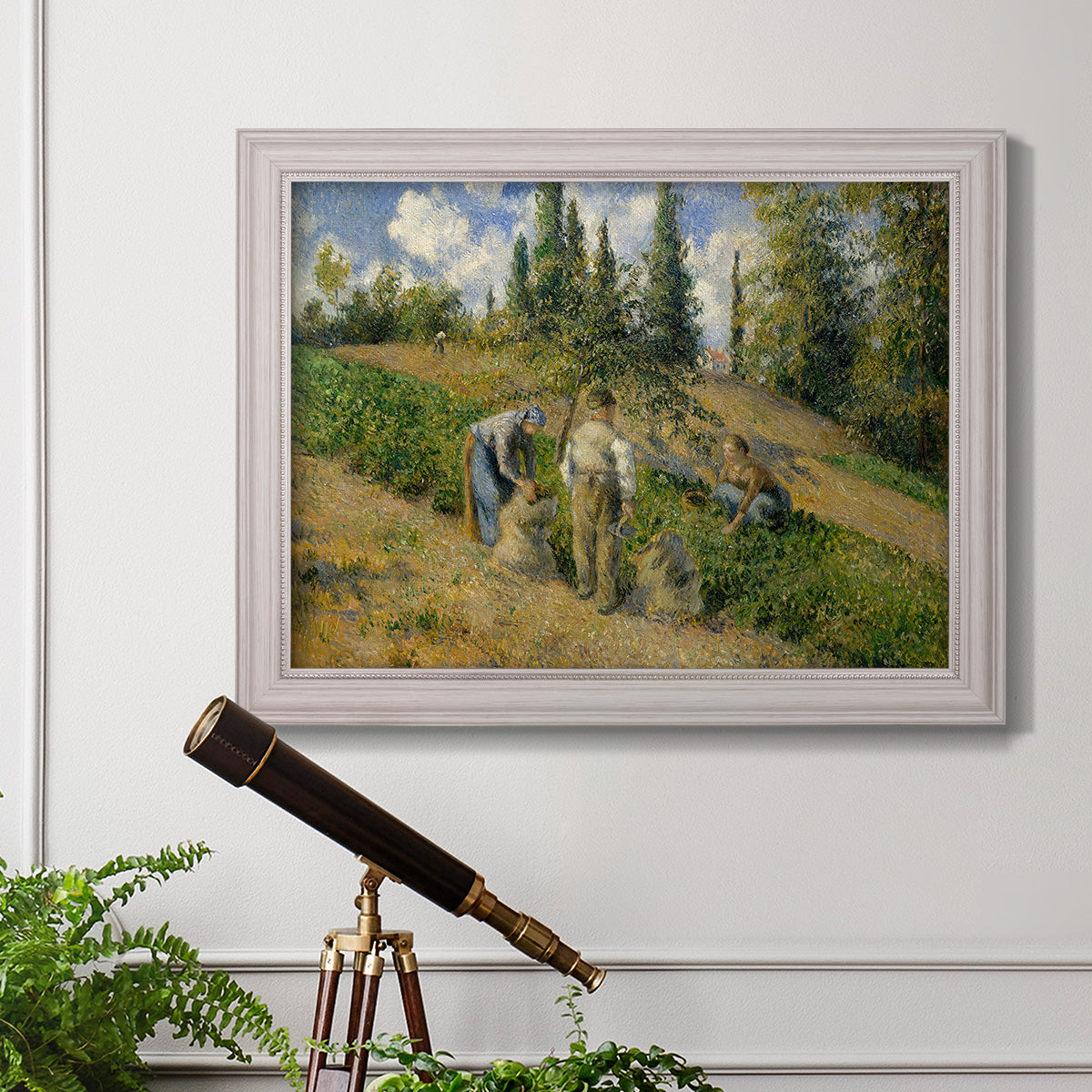 Impressionist countryside harvest scene by Camille Pissarro in an ornate weathered white frame displayed in a light-toned interior setting.
