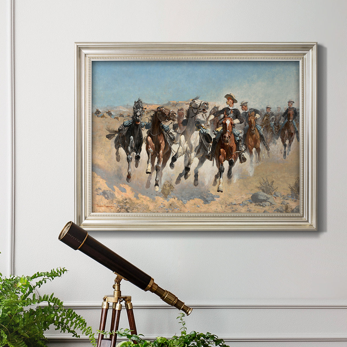Impressionist western action scene by Frederic Remington in an ornate champagne frame displayed in a light-toned interior setting.