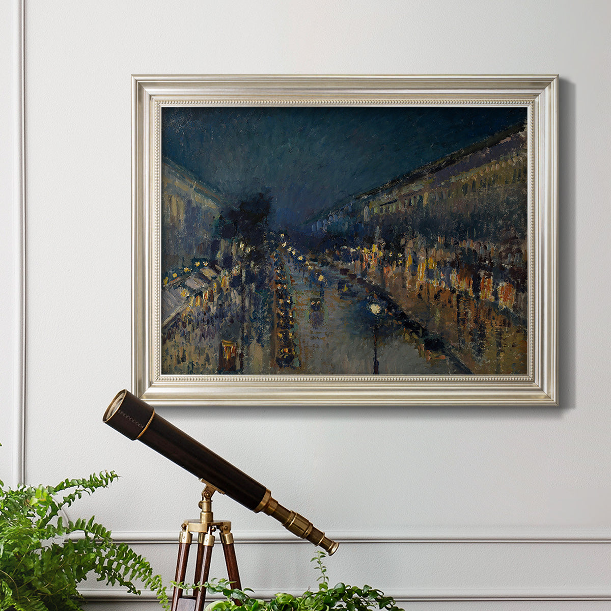 Impressionist nighttime Paris street scene by Camille Pissarro in an ornate champagne frame displayed in a light-toned interior setting.