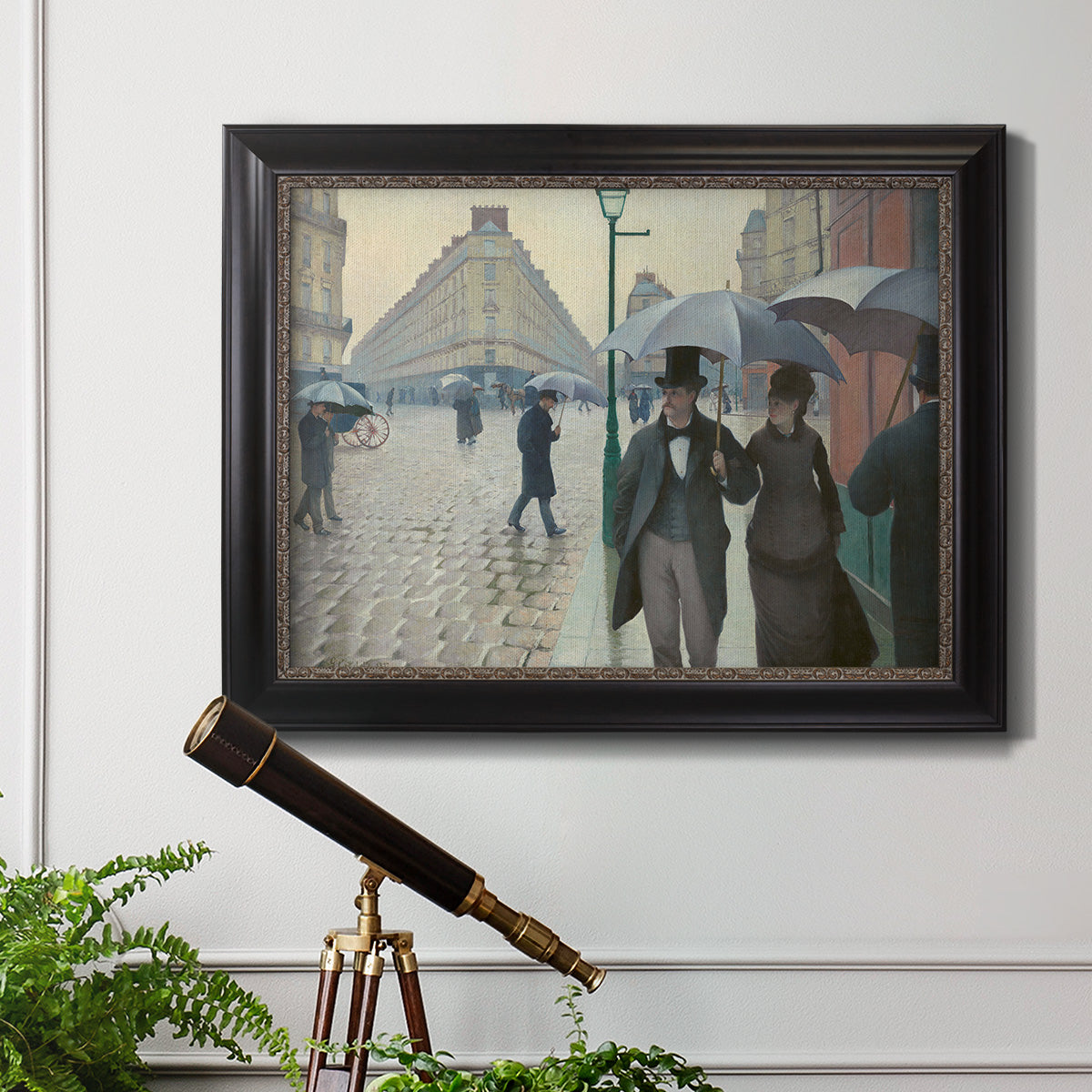 Impressionist urban street scene in the rain by Gustave Caillebotte in an ornate black frame with gilded inner detail displayed in a light-toned interior setting.