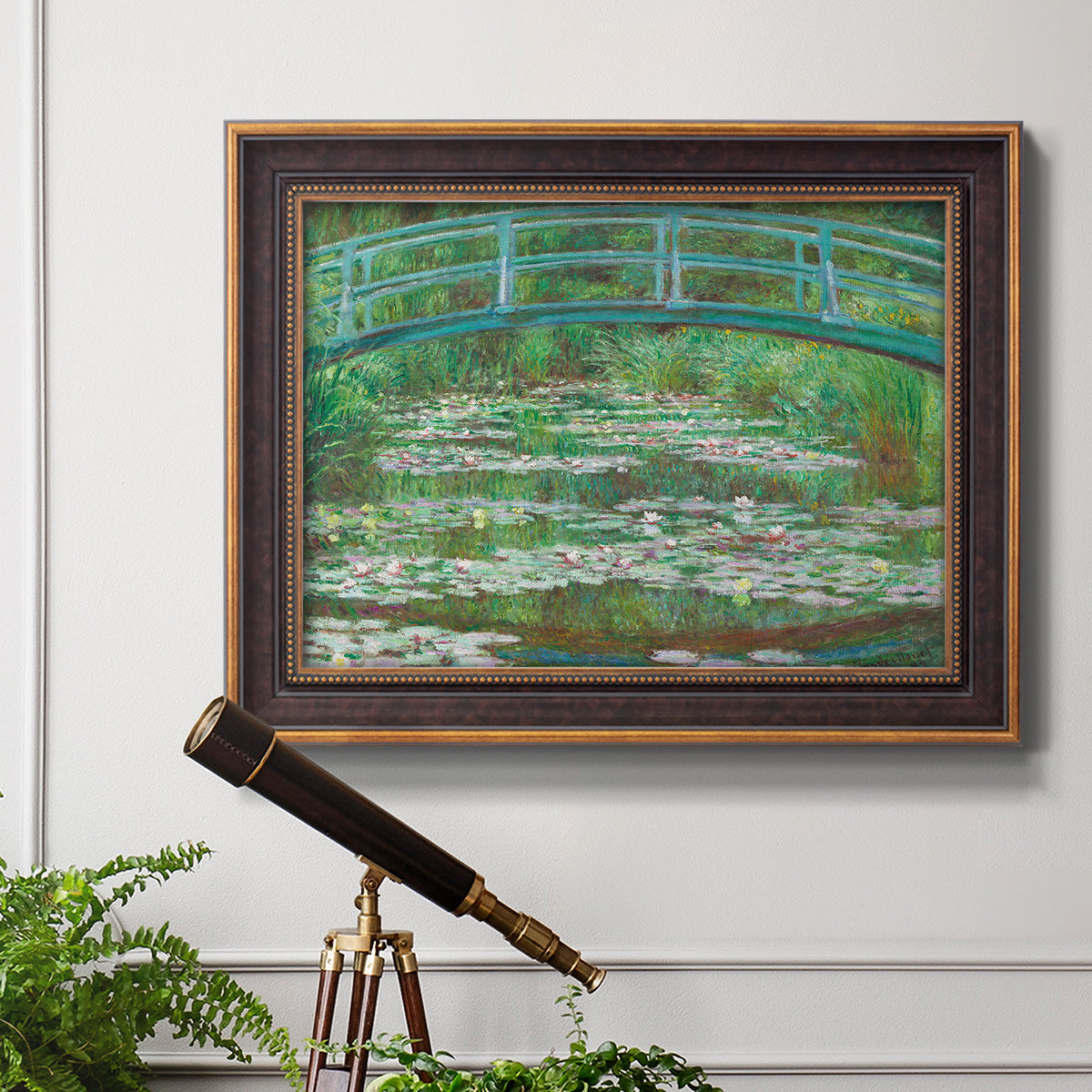 Impressionist garden scene with Japanese bridge and water lilies by Claude Monet in an ornate bronzed mahogany wood frame displayed in a light-toned interior setting.