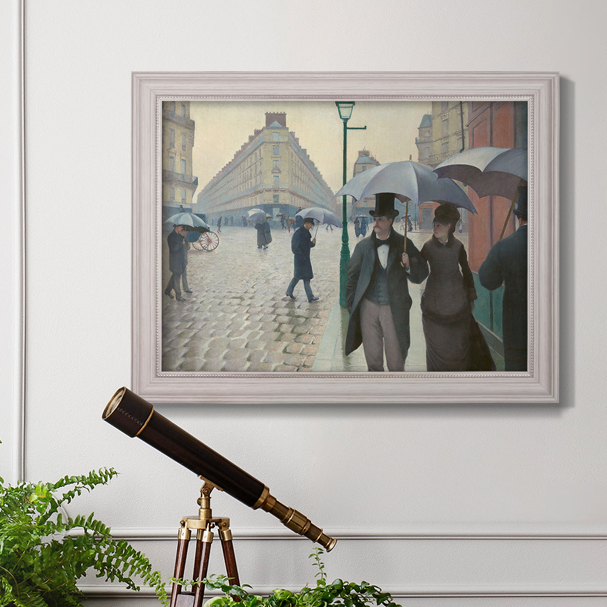 Impressionist urban street scene in the rain by Gustave Caillebotte in an ornate weathered white frame displayed in a light-toned interior setting.