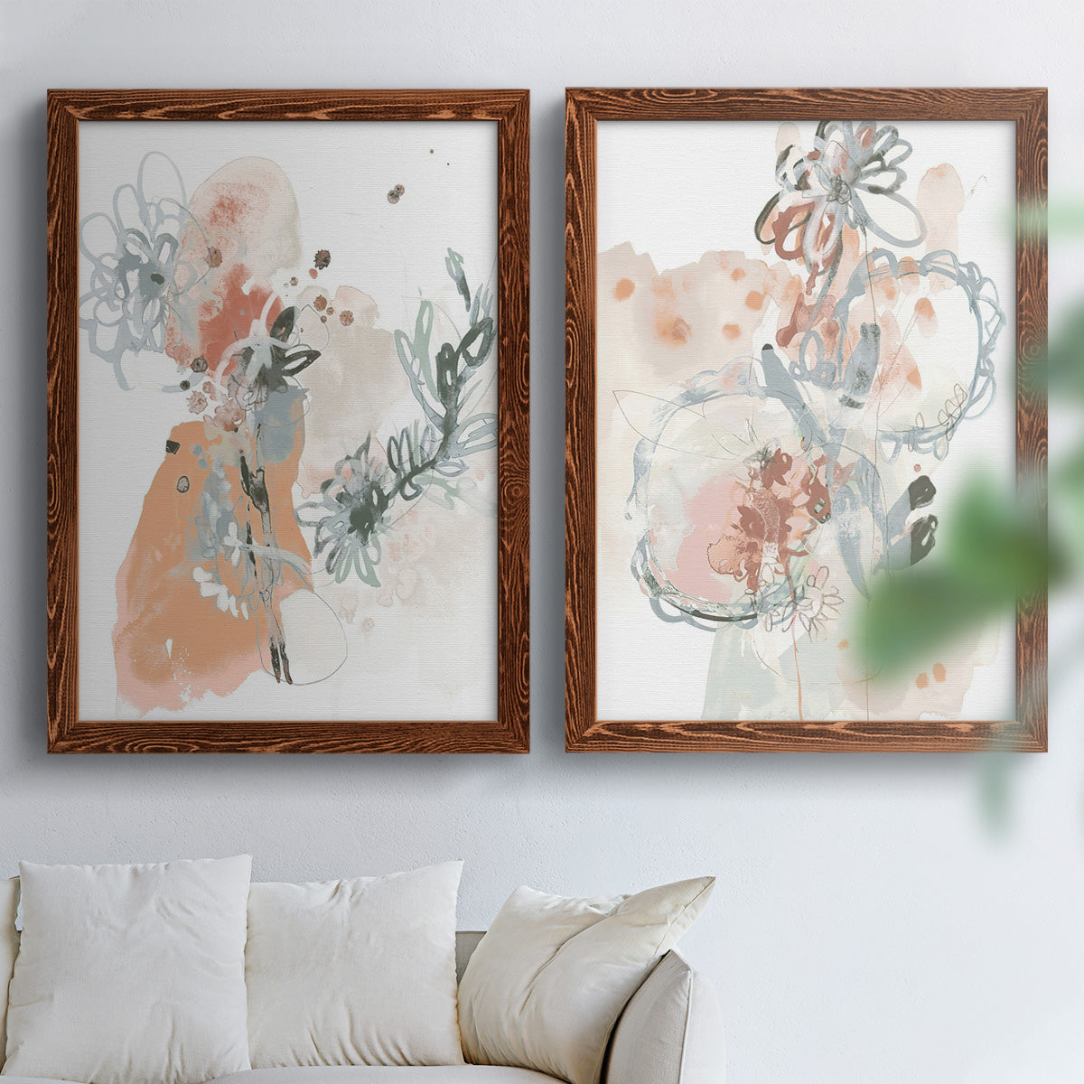 Set of two maple barnwood framed canvas prints depicting scribbled petals, translucent washes, and drifting stems arranged across two complementary compositions above a sofa in a bright living space.