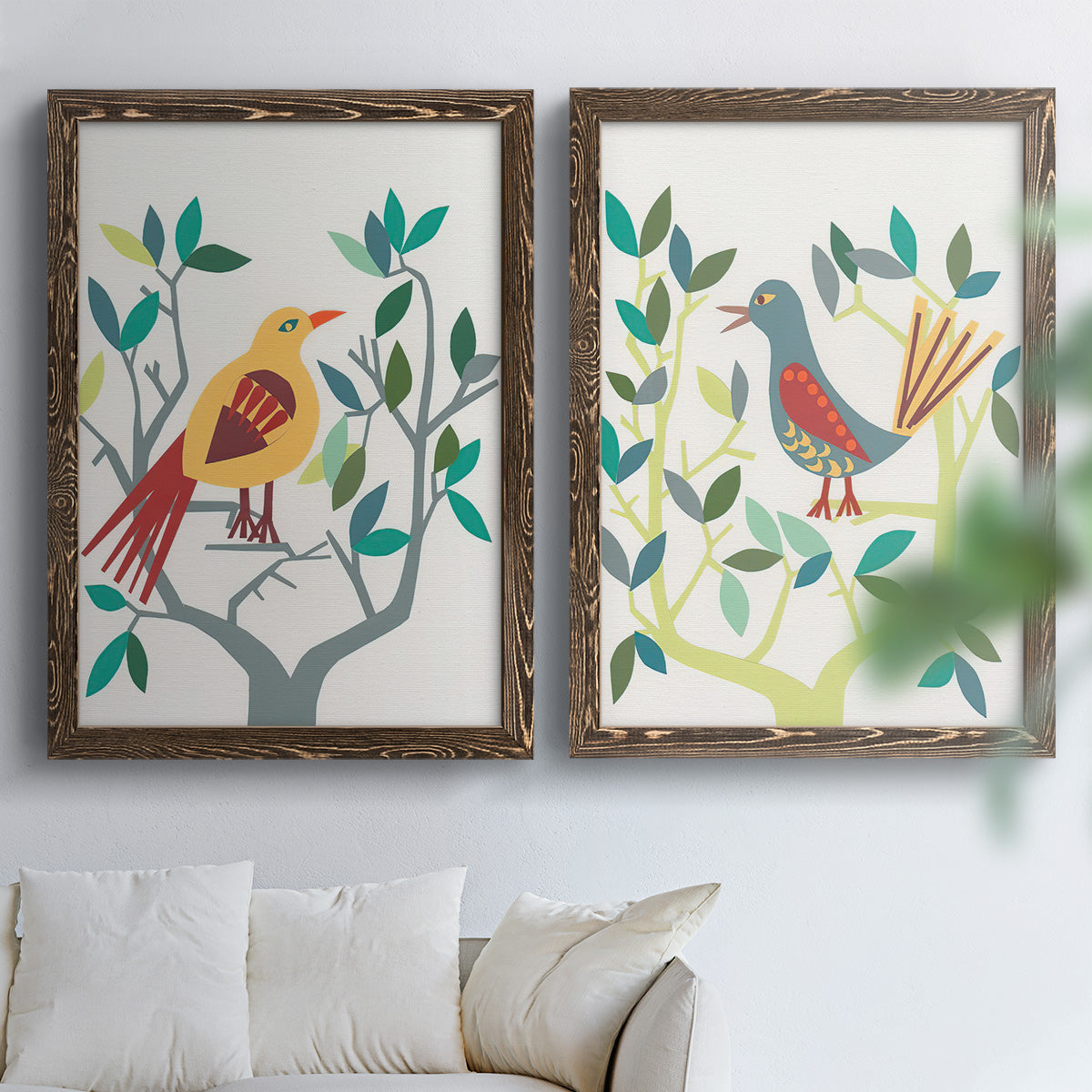 Set of two walnut barnwood framed canvas prints depicting red yellow blue plumage, simplified leaves, and playful flat shapes arranged across two complementary compositions above a sofa in a bright living space.