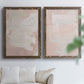 Set of two walnut barnwood framed canvas prints depicting cloudy rose washes, broad pale strokes, and subtle texture arranged across two complementary compositions above a sofa in a bright living space.
