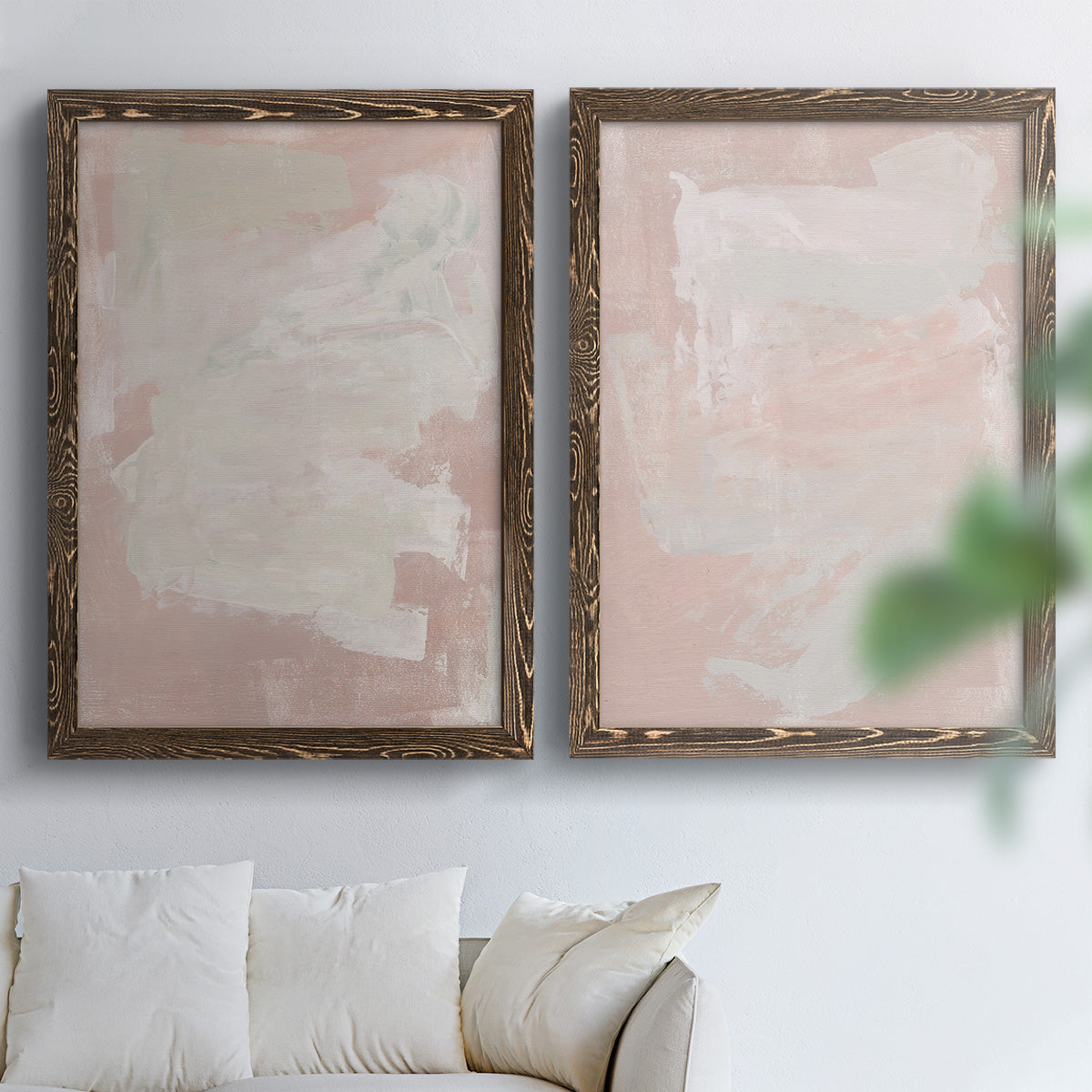 Set of two walnut barnwood framed canvas prints depicting cloudy rose washes, broad pale strokes, and subtle texture arranged across two complementary compositions above a sofa in a bright living space.