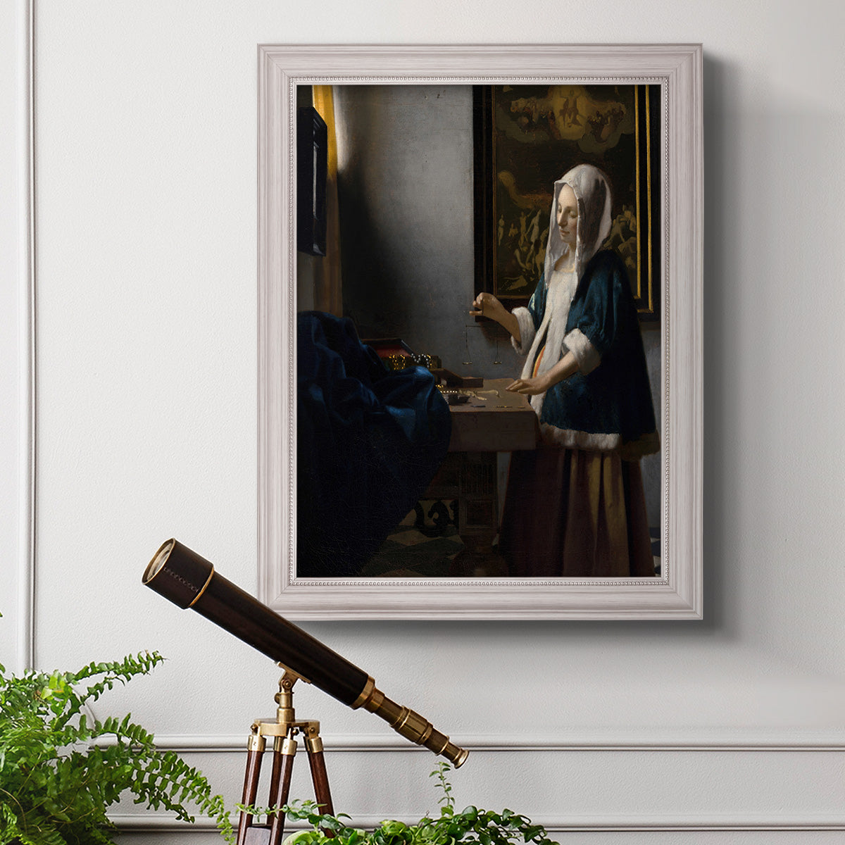 Quiet interior genre scene of a woman with scales by Johannes Vermeer in an ornate weathered white frame displayed in a light-toned interior setting.