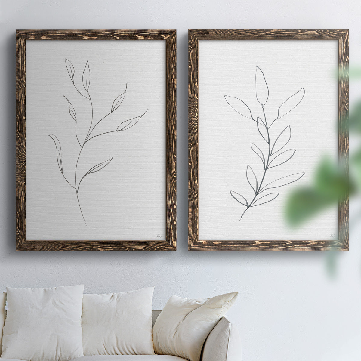 Set of two walnut barnwood framed canvas prints depicting thin gray contours, sparse stems, and clean white fields arranged across two complementary compositions above a sofa in a bright living space.