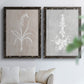 Set of two black barnwood framed canvas prints depicting delicate stems, leaves, and blossoms against gray taupe and pale blue panels arranged across two complementary compositions above a sofa in a bright living space.