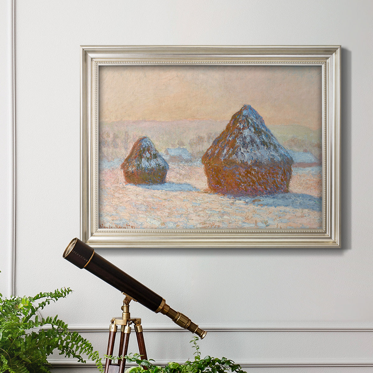 Impressionist winter haystack scene by Claude Monet in an ornate champagne frame displayed in a light-toned interior setting.