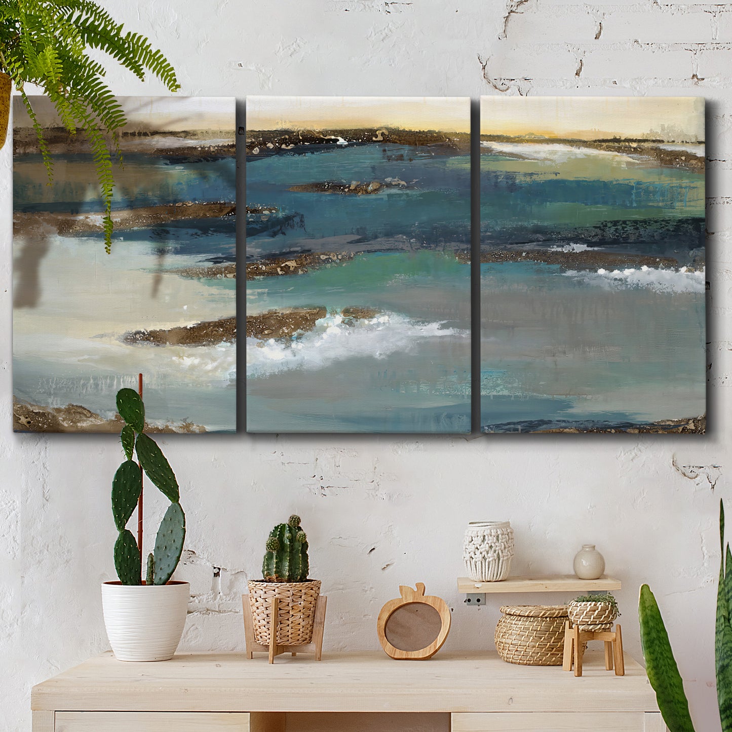 Three-panel canvas wall art featuring rocky coastal bluff above sea, displayed in a boho-chic entryway above a console table.