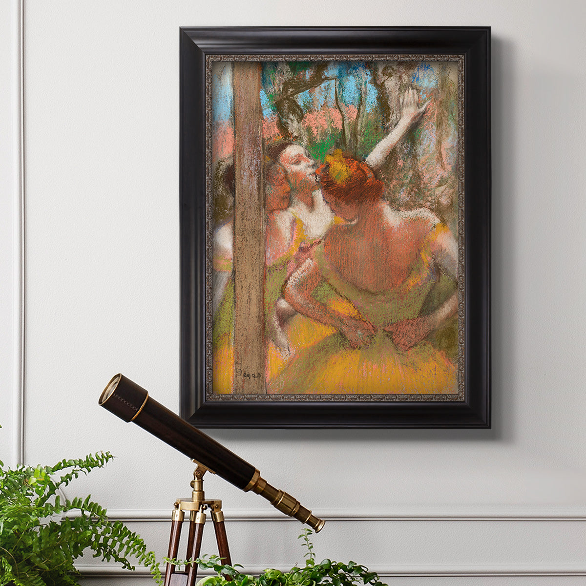 Impressionist ballet dancer composition by Edgar Degas in an ornate black frame with gilded inner detail displayed in a light-toned interior setting.