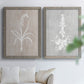 Set of two gray barnwood framed canvas prints depicting delicate stems, leaves, and blossoms against gray taupe and pale blue panels arranged across two complementary compositions above a sofa in a bright living space.