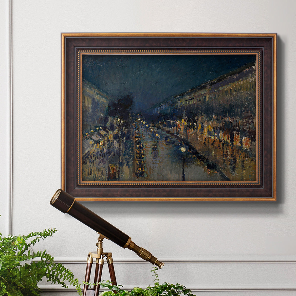 Impressionist nighttime Paris street scene by Camille Pissarro in an ornate bronzed mahogany wood frame displayed in a light-toned interior setting.