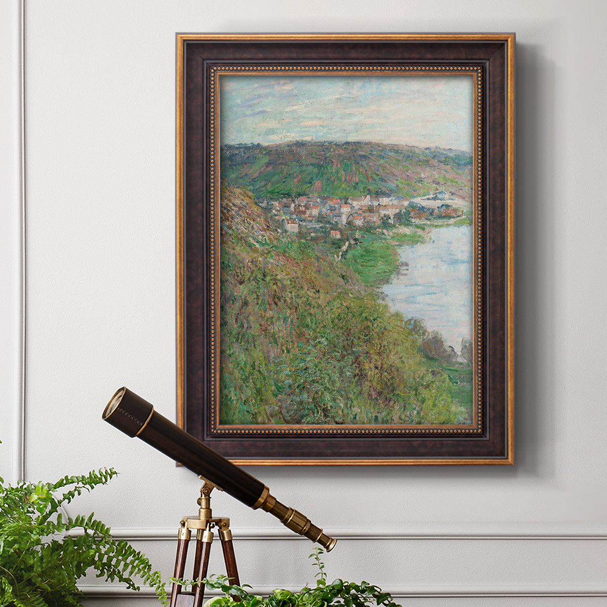 Impressionist landscape view of Vétheuil by Claude Monet in an ornate bronzed mahogany wood frame displayed in a light-toned interior setting.