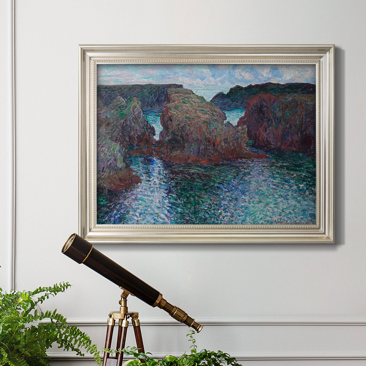 Impressionist rocky seascape by Claude Monet in an ornate champagne frame displayed in a light-toned interior setting.