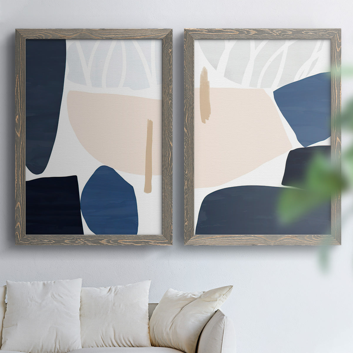 Set of two gray barnwood framed canvas prints depicting rounded dark forms, pale sand fields, and clean modern edges arranged across two complementary compositions above a sofa in a bright living space.