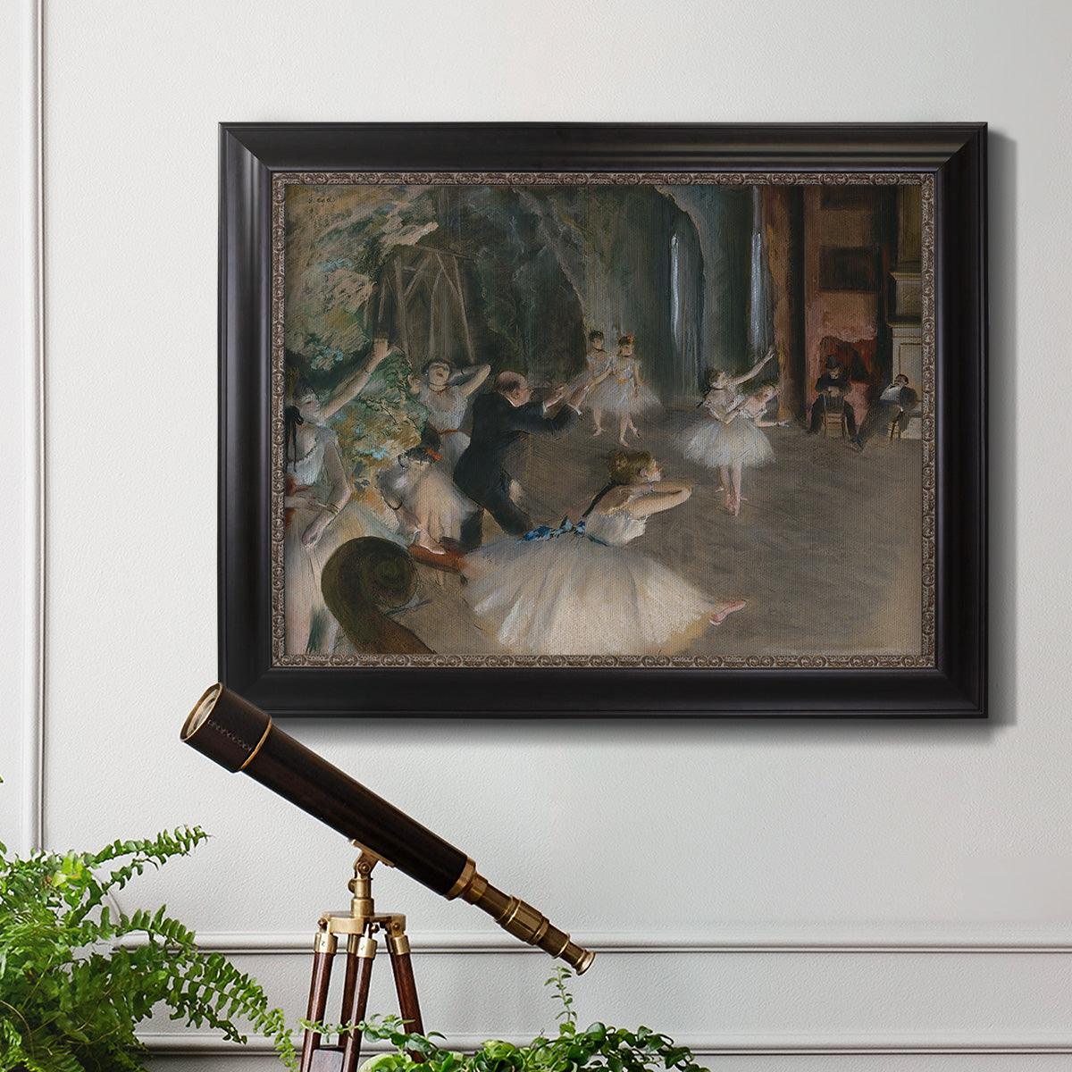Impressionist backstage ballet scene by Edgar Degas in an ornate black frame with gilded inner detail displayed in a light-toned interior setting.