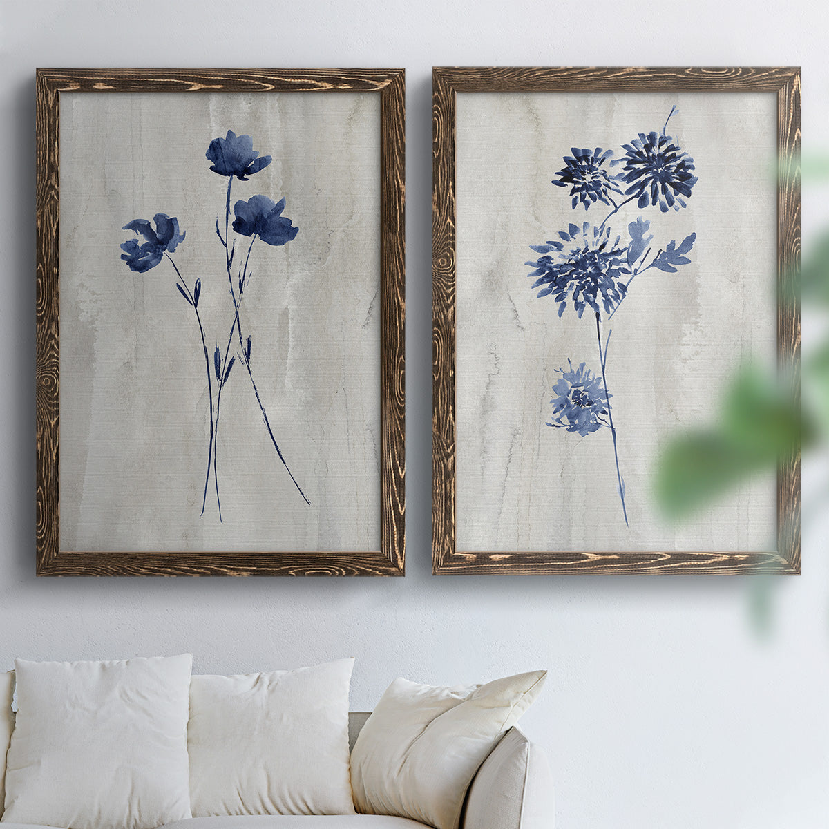 Set of two walnut barnwood framed canvas prints depicting indigo blossoms, thin stems, and softly distressed gray backgrounds arranged across two complementary compositions above a sofa in a bright living space.