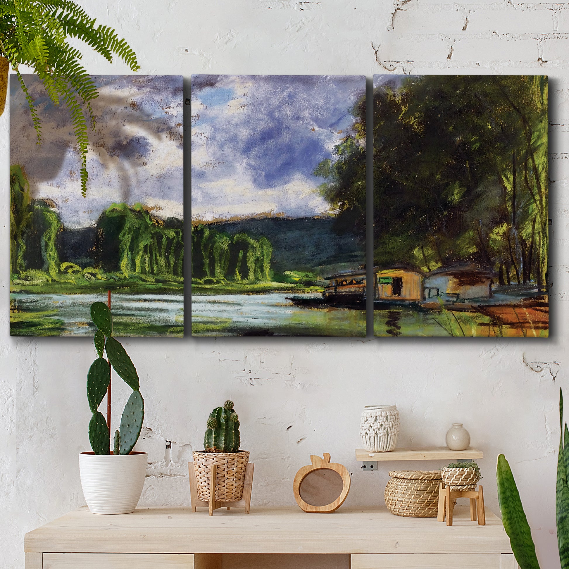 Three-panel canvas wall art featuring riverbank landscape near village, displayed in a boho-chic entryway above a console table.