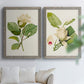 Set of two gray barnwood framed canvas prints depicting large pale petals, leafy branches, and soft watercolor shading arranged across two complementary compositions above a sofa in a bright living space.