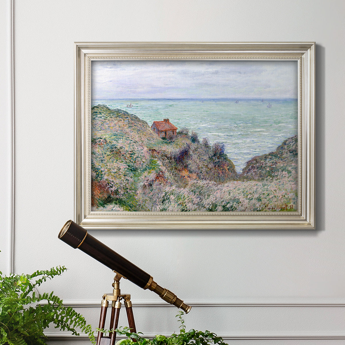 Impressionist coastal watch cabin scene by Claude Monet in an ornate champagne frame displayed in a light-toned interior setting.