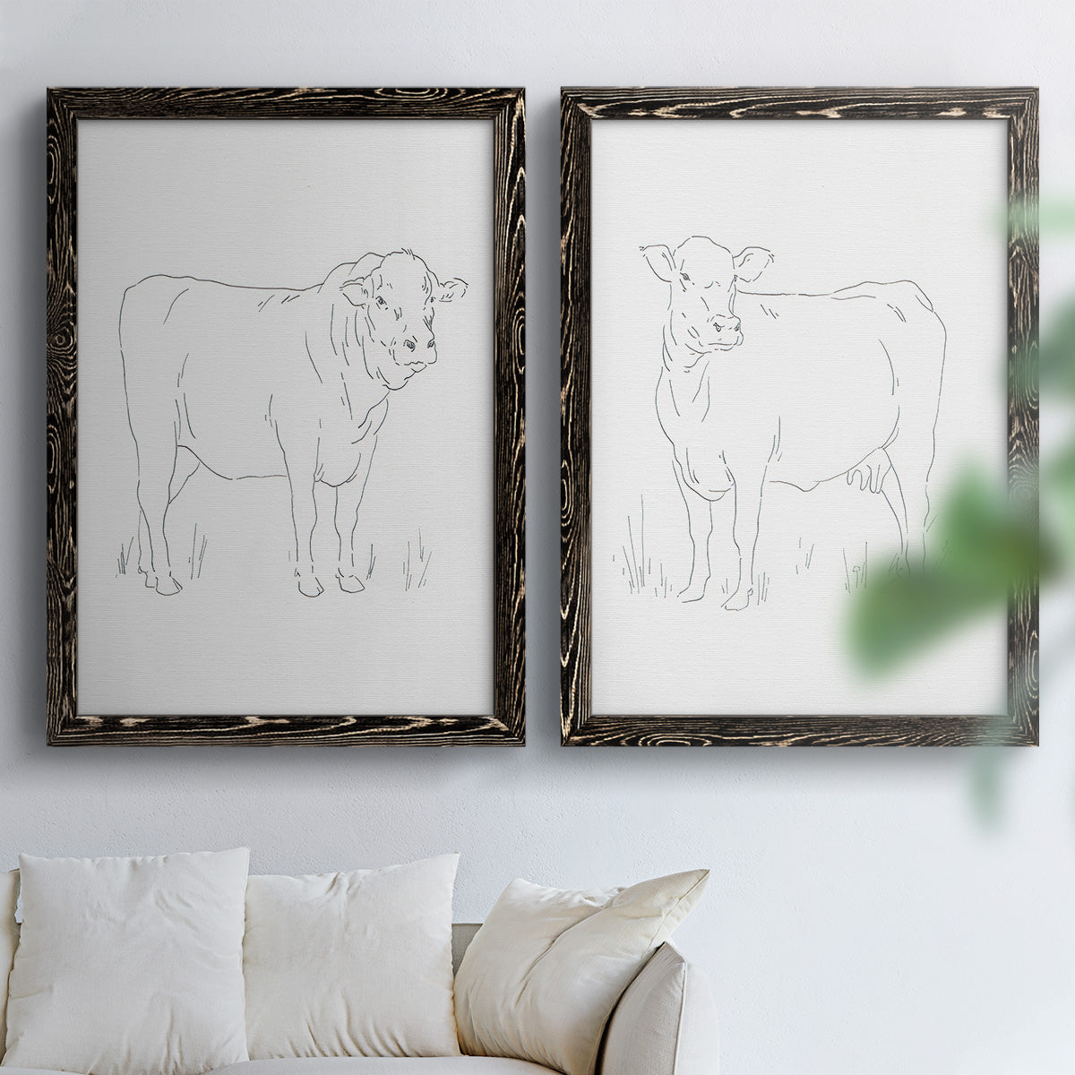 Set of two black barnwood framed canvas prints depicting fine gray lines, white backgrounds, and quiet farm-animal profiles arranged across two complementary compositions above a sofa in a bright living space.