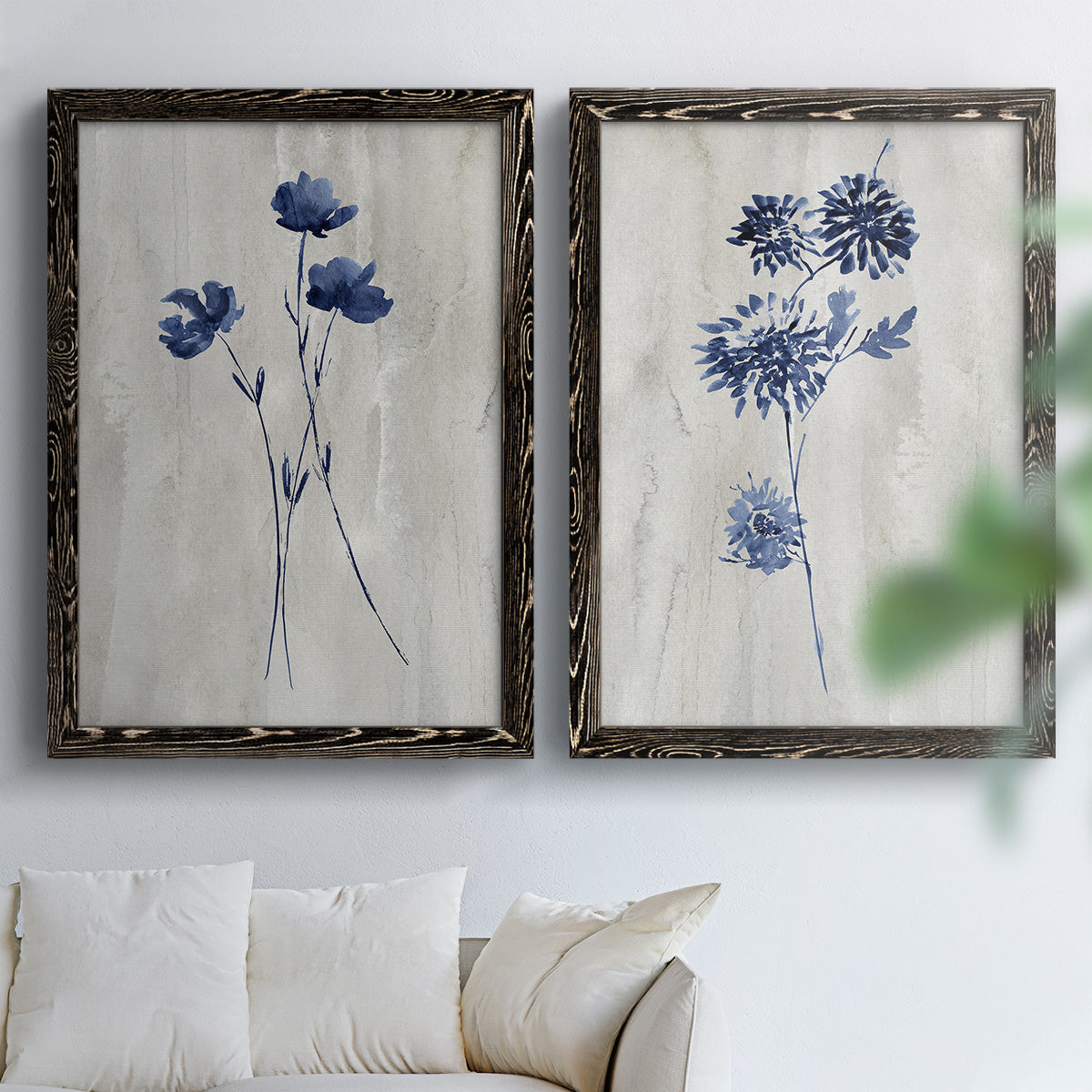 Set of two black barnwood framed canvas prints depicting indigo blossoms, thin stems, and softly distressed gray backgrounds arranged across two complementary compositions above a sofa in a bright living space.