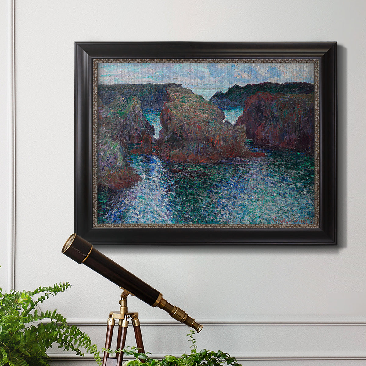 Impressionist rocky seascape by Claude Monet in an ornate black frame with gilded inner detail displayed in a light-toned interior setting.