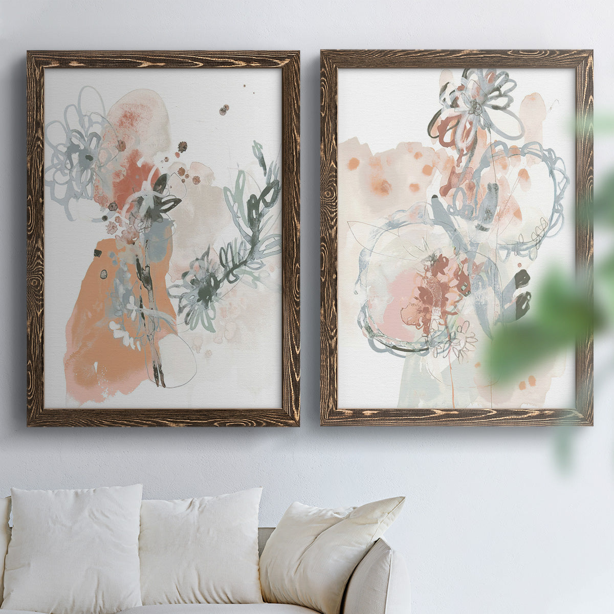 Set of two walnut barnwood framed canvas prints depicting scribbled petals, translucent washes, and drifting stems arranged across two complementary compositions above a sofa in a bright living space.
