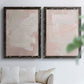 Set of two black barnwood framed canvas prints depicting cloudy rose washes, broad pale strokes, and subtle texture arranged across two complementary compositions above a sofa in a bright living space.