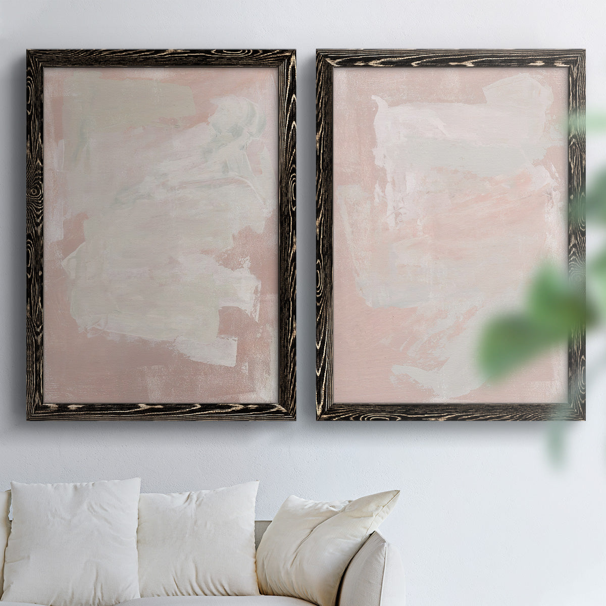 Set of two black barnwood framed canvas prints depicting cloudy rose washes, broad pale strokes, and subtle texture arranged across two complementary compositions above a sofa in a bright living space.