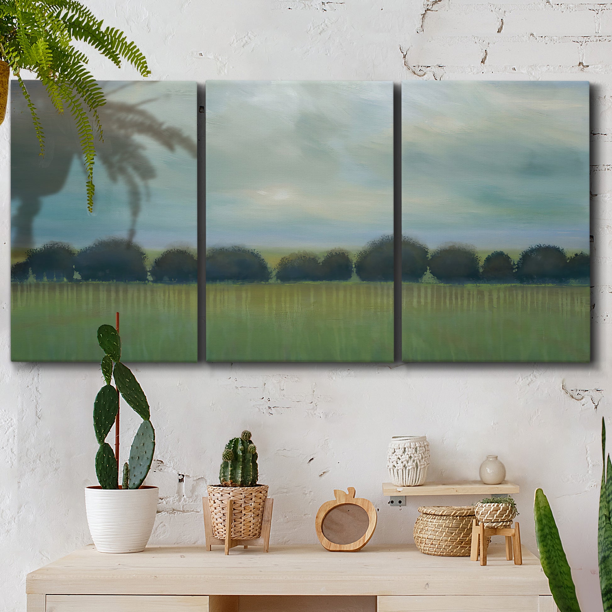 Three-panel canvas wall art featuring rolling green pastoral fields, displayed in a boho-chic entryway above a console table.